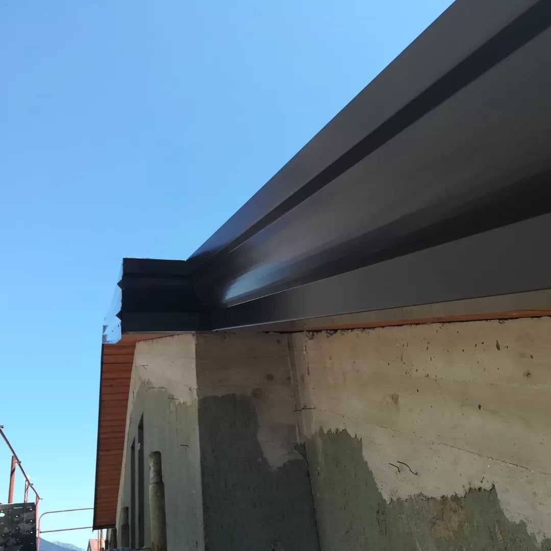 Dal basso, contro il cielo: la gronda scura sul muro in ripresa, con la sua faccia a gradini e la testata all’angolo.