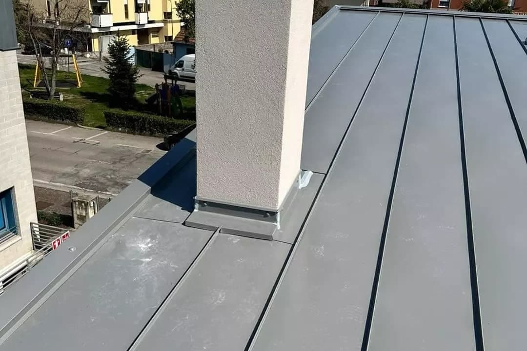 La copertura aggraffata finita: lastre grigie con le nervature in rilievo e il camino rifinito alla base.