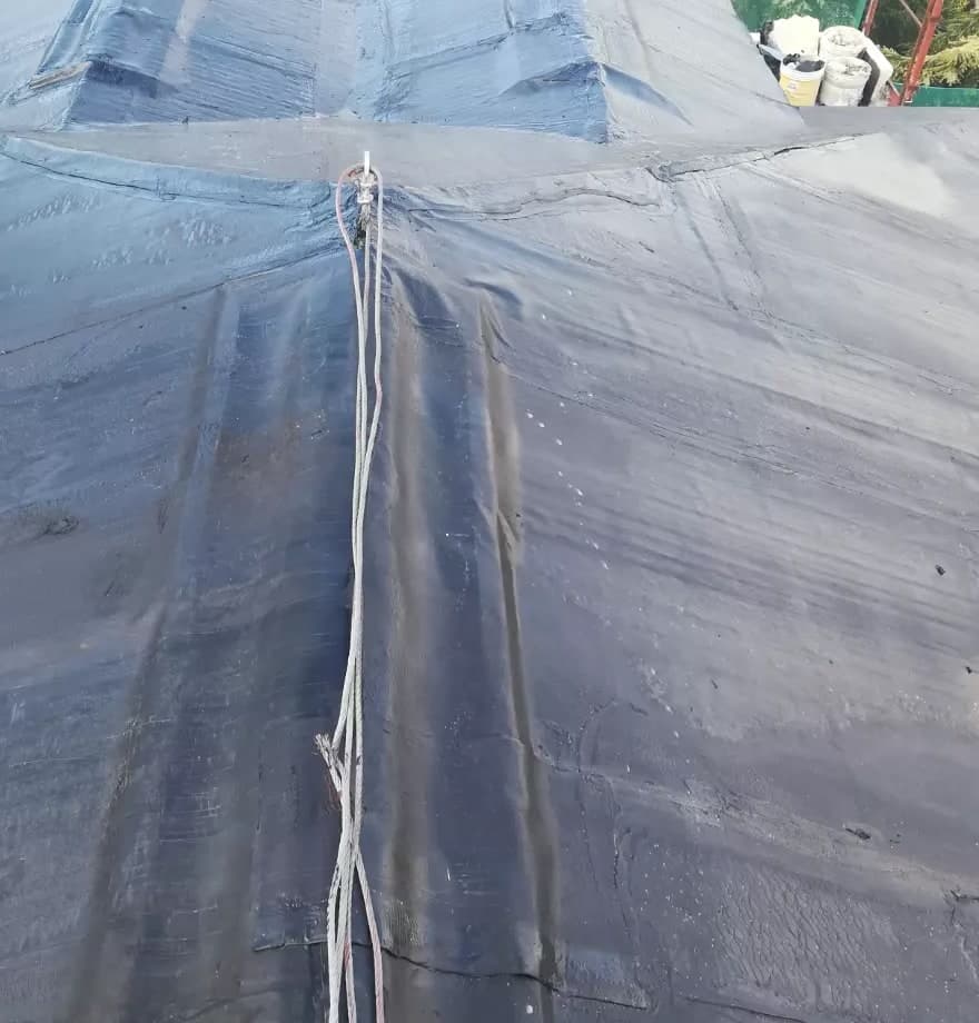 Dall’alto, il colmo in guaina nera, con la fune di sicurezza del cantiere, corre fino al colmo di traverso del tetto più grande; in alto a destra il ponteggio.
