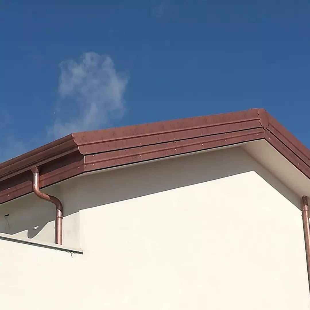 L’angolo di un tetto visto dal basso: la gronda color rame a gradini gira l’angolo, e un pluviale tondo scende lungo il muro.