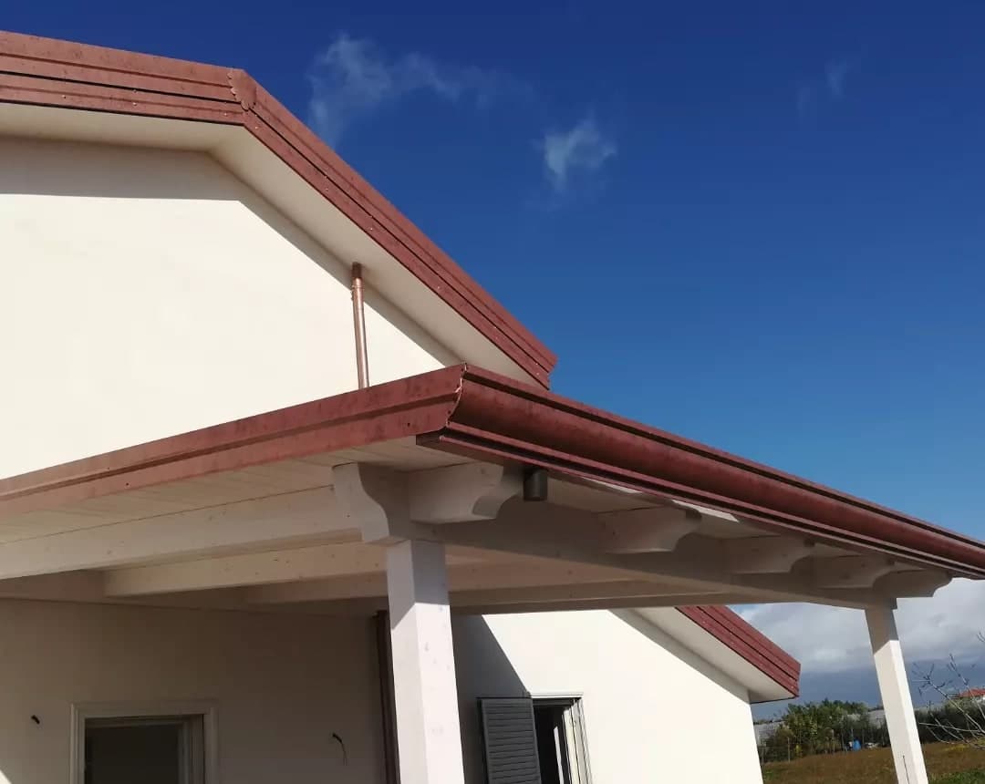 Il portico su colonne bianche, con la gronda «a cornice» color rame e i travetti bianchi a vista; sopra, il timpano.