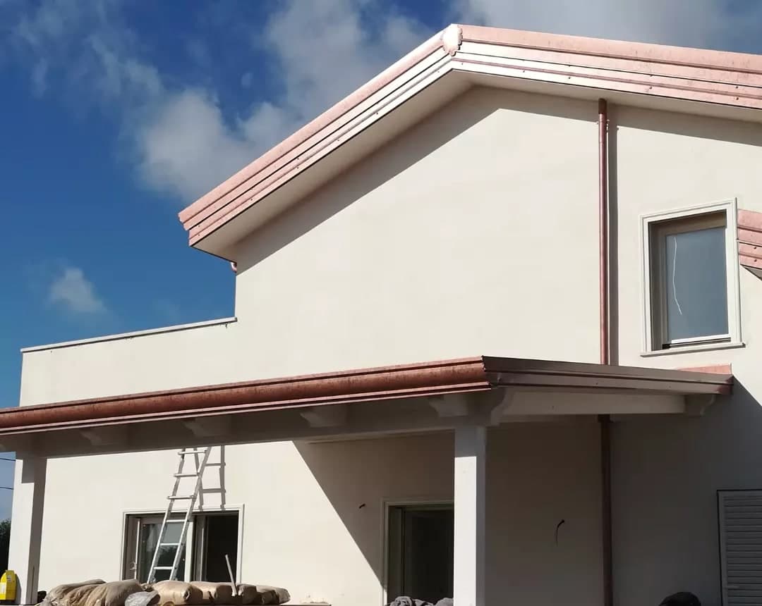 Il timpano della villa: lungo i due spioventi la lamiera color rame a gradini, come la gronda; sotto, il portico con la sua gronda e una colonna bianca.