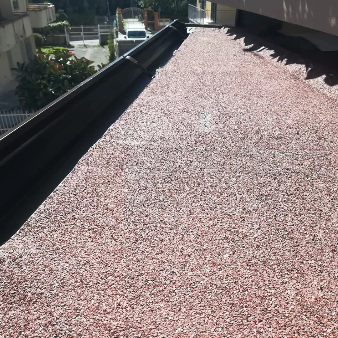 Il tetto della tettoia dall’alto: la guaina rossa a graniglia grossa, la gronda testa di moro lungo il bordo, con una staffa nella bocca, che in fondo gira l’angolo; sotto, il cortile.