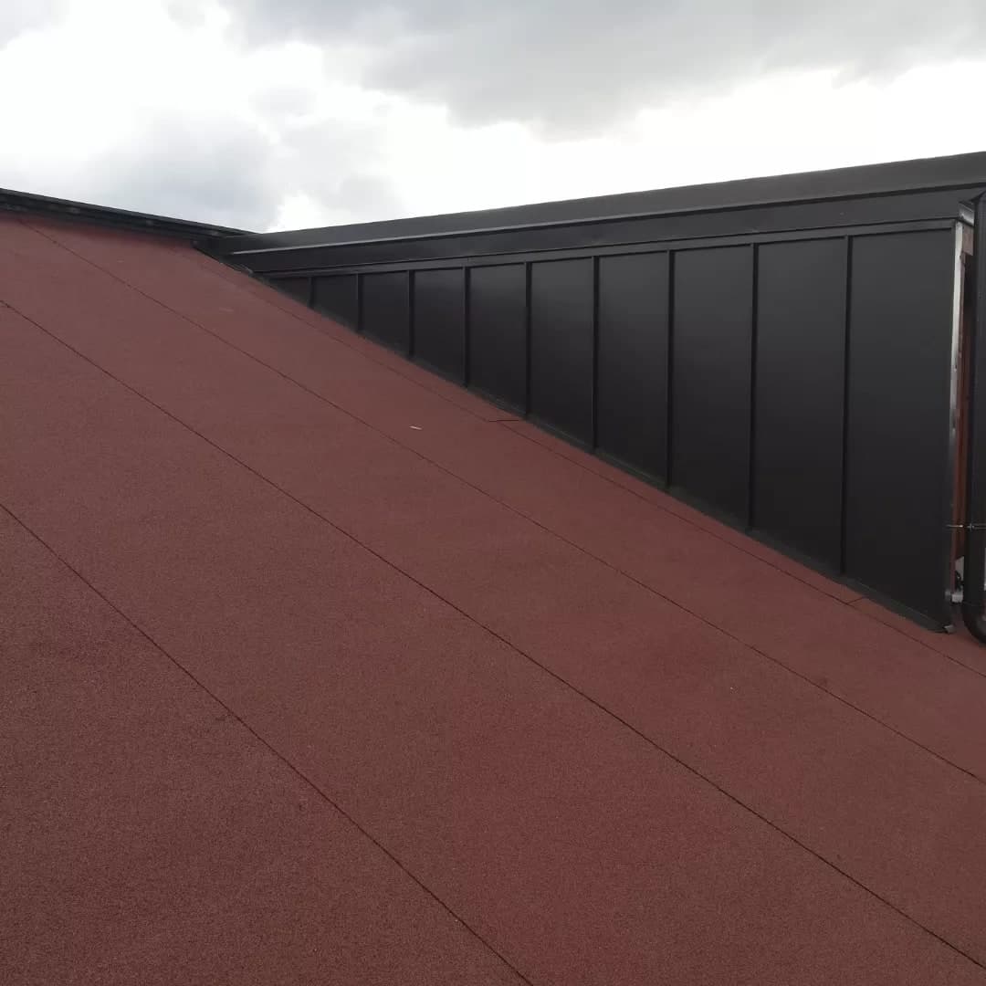 La parete di un abbaino vista lungo la falda: doghe verticali in lamiera scura aggraffata, che scendono fino alla guaina rossa.