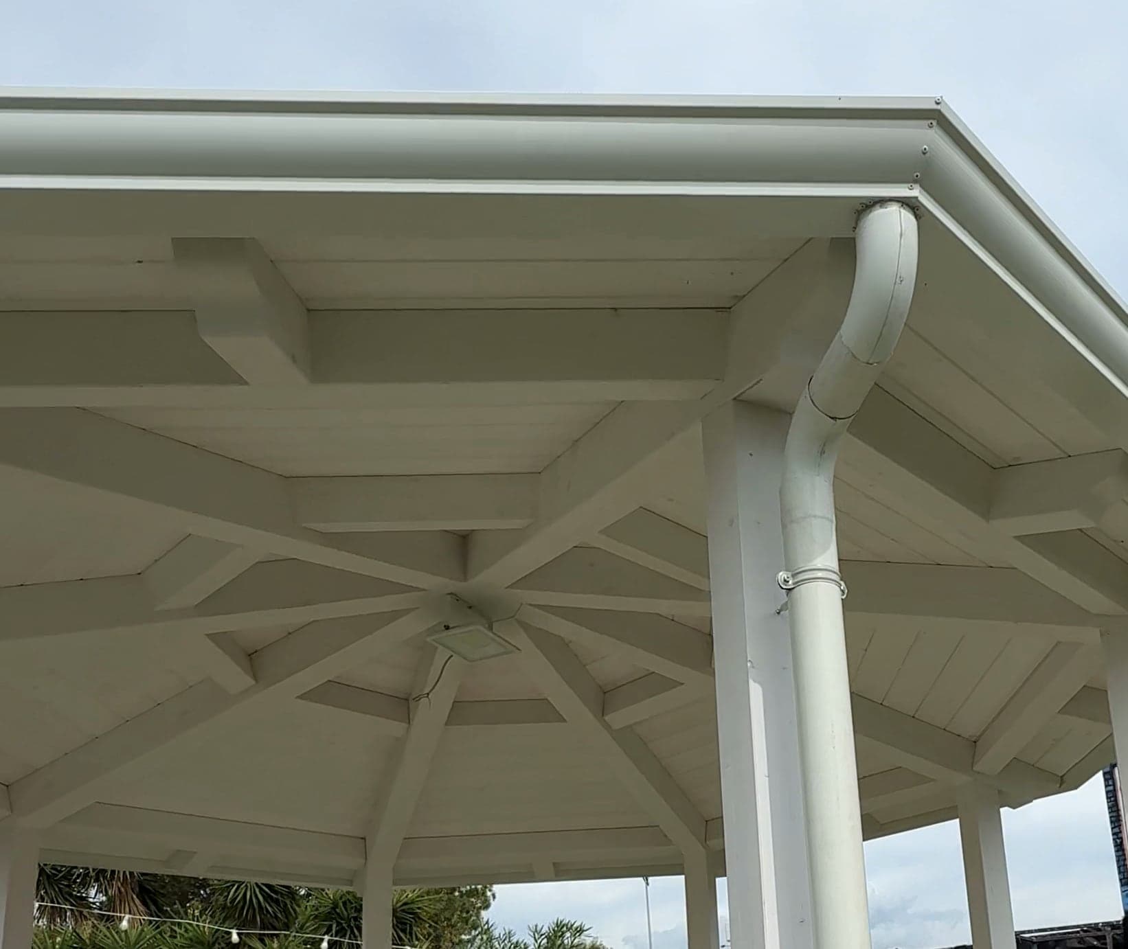 Uno spigolo del gazebo visto da sotto: la gronda bianca unita ad angolo con i rivetti, e il pluviale tondo che con due curve raggiunge il pilastro e scende, tenuto da un collare.