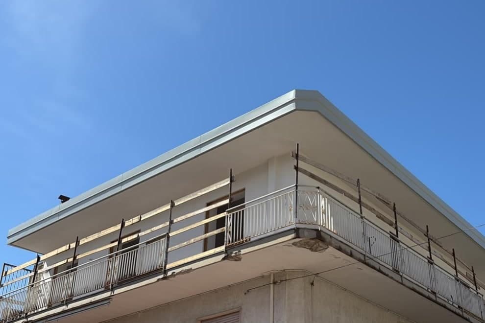 Dopo i lavori: lo stesso edificio con il bordo della copertura rifatto e rifinito in lamiera chiara.