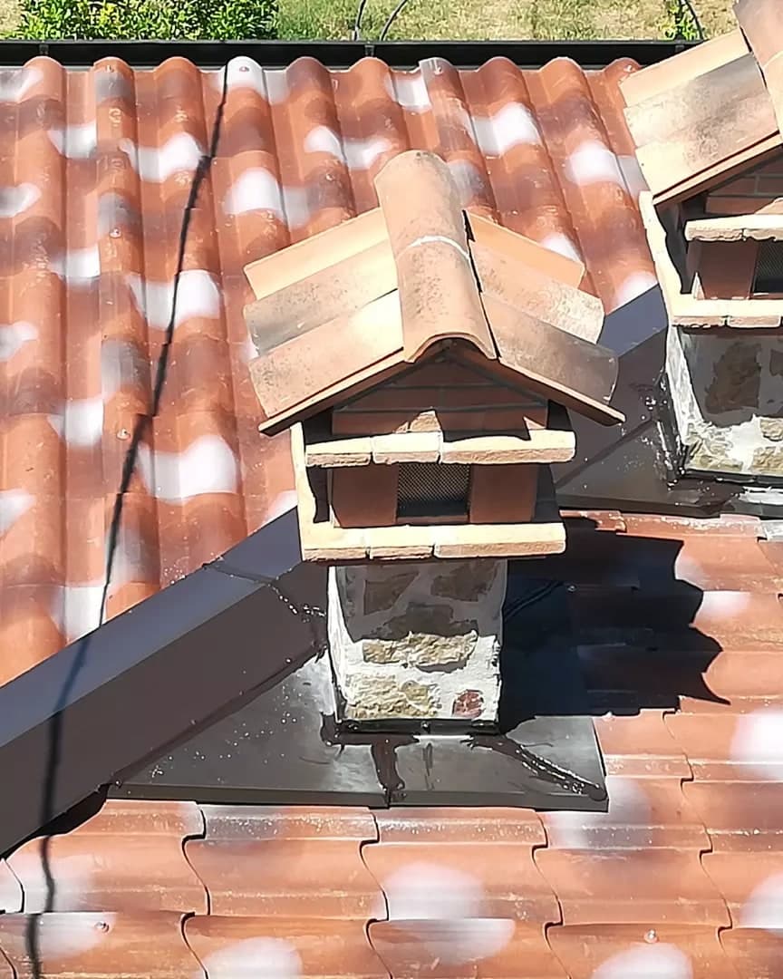 Due camini su un tetto: alla base di ciascuno una lamiera scura sagomata raccorda il camino al manto.