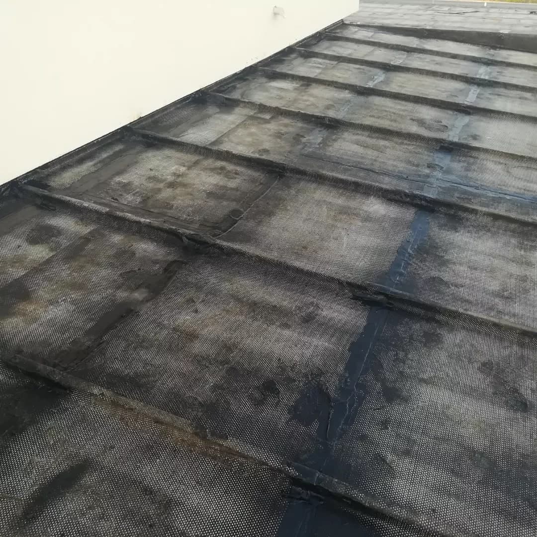 Il primo strato di guaina nera sulla tettoia, a teli saldati, contro il muro bianco della palazzina.