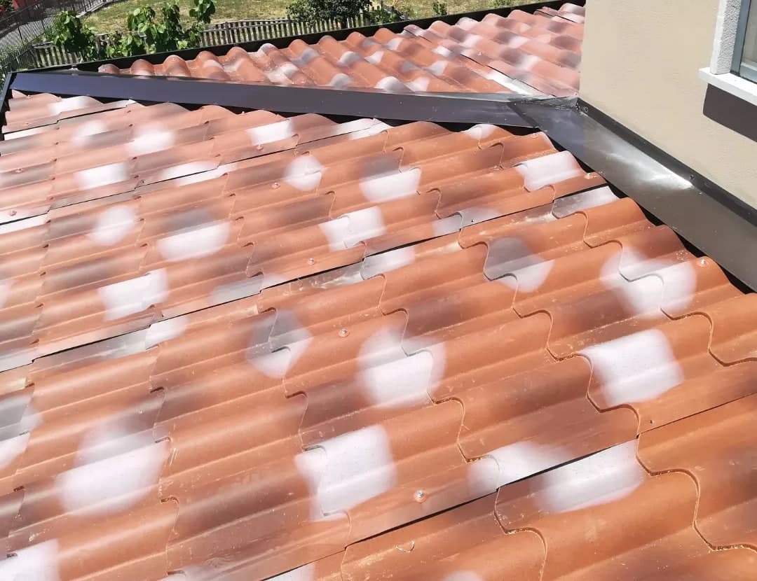 Il displuvio che sale al muro della casa: il cappello scuro, la scossalina contro il muro lungo il bordo alto della falda, le lastre finto coppo; a destra la finestra con il davanzale.