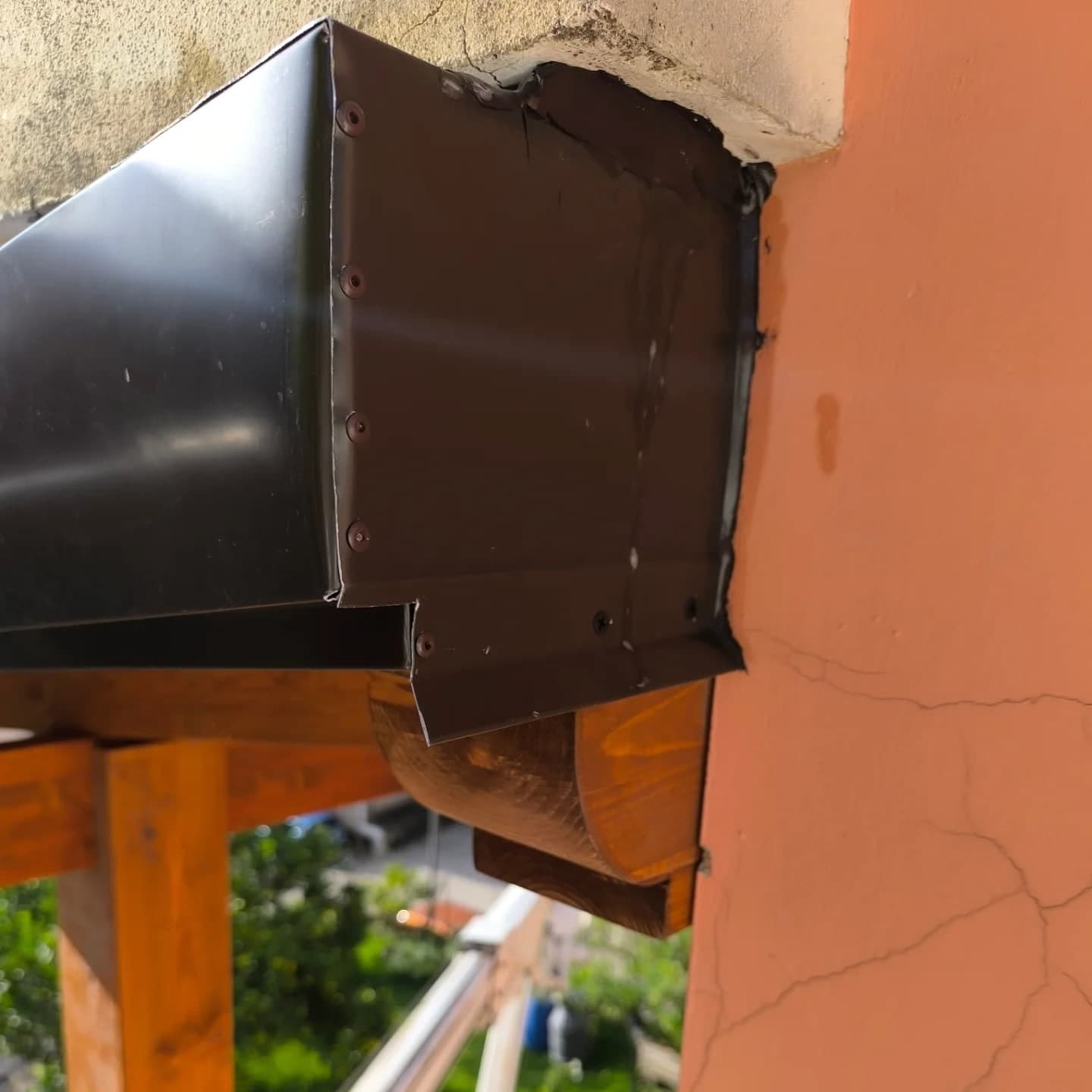 Da vicino: la testata della gronda scura, rivettata, dove il canale arriva contro il muro.