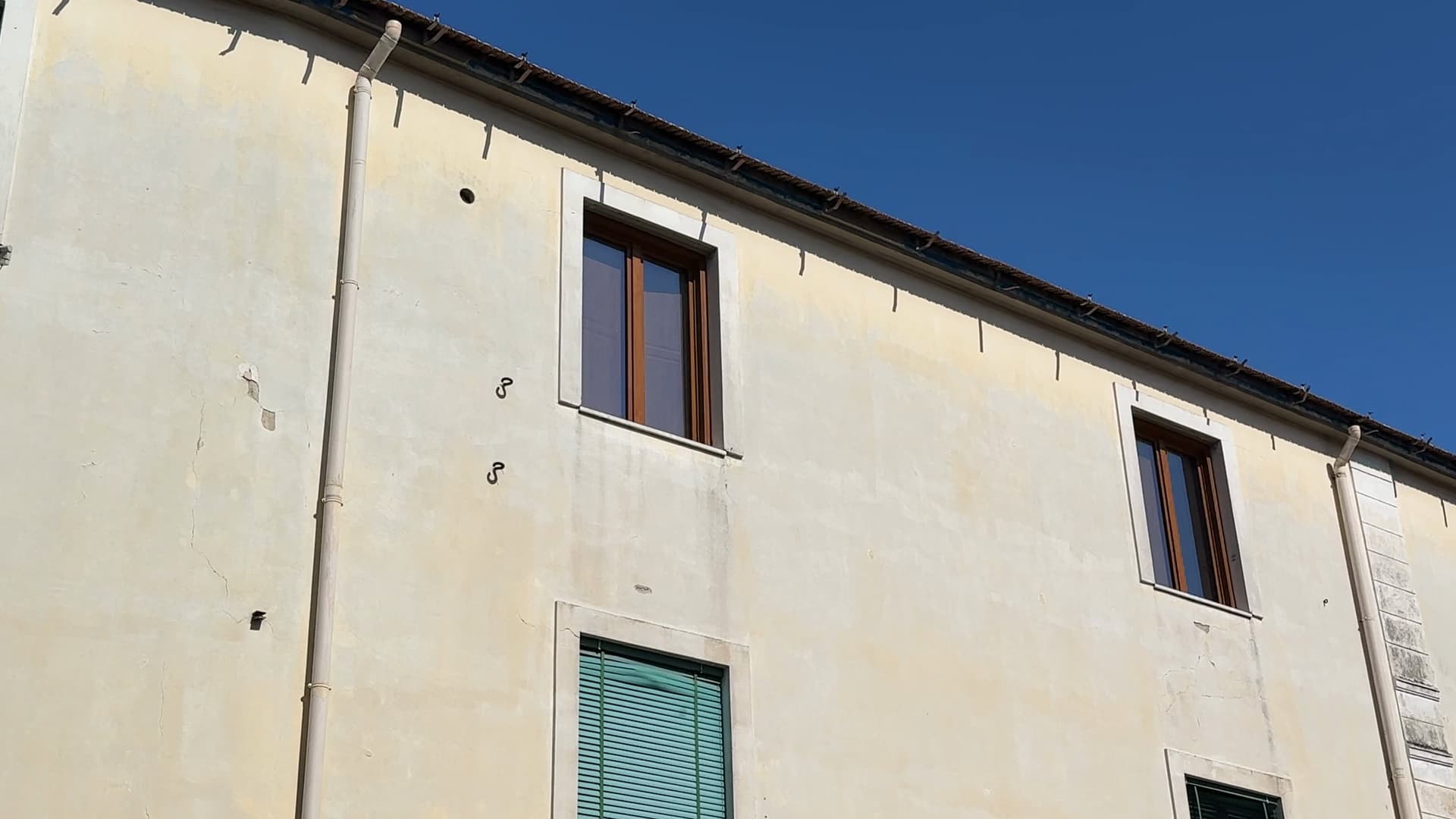 Prima dei lavori: la facciata di un edificio vista dal basso, con la vecchia gronda lungo il bordo del tetto, appesa a staffe a gancio.