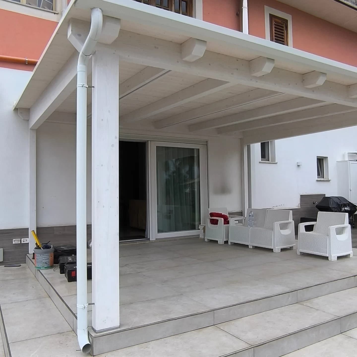 Tettoia in legno verniciata di bianco, con gronda e pluviale bianchi: lo scarico scende lungo il pilastro.