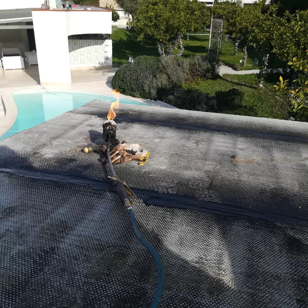 Sul tetto della pergola il primo strato di guaina nera, a teli, con il cannello ancora acceso; sotto, la piscina e il giardino con gli agrumi.