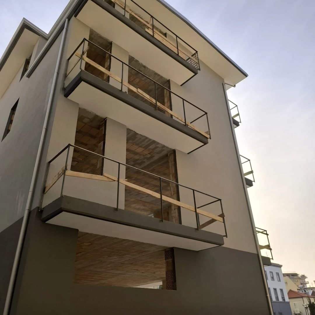 L’angolo della palazzina da sotto: la gronda grigio chiaro che gira l’angolo della soletta, i pluviali lungo gli spigoli, i balconi e lo zoccolo grigio scuro.