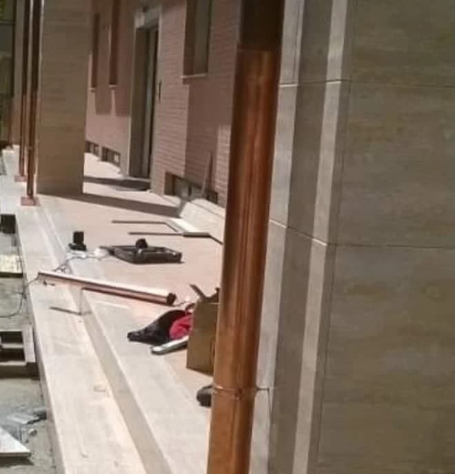 Il portico guardato lungo i pilastri rivestiti di pietra chiara: davanti a ognuno un pluviale di rame nuovo; dietro, il muro in mattoni a vista con il portone; sul pavimento gli attrezzi del cantiere.