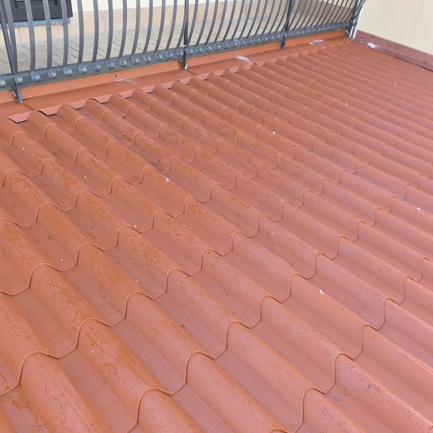 Dall’alto, le lastre finto coppo color cotto avvitate; sotto la ringhiera del balcone la chiusura dentata come le onde, contro il muro dell’ala la scossalina marrone.