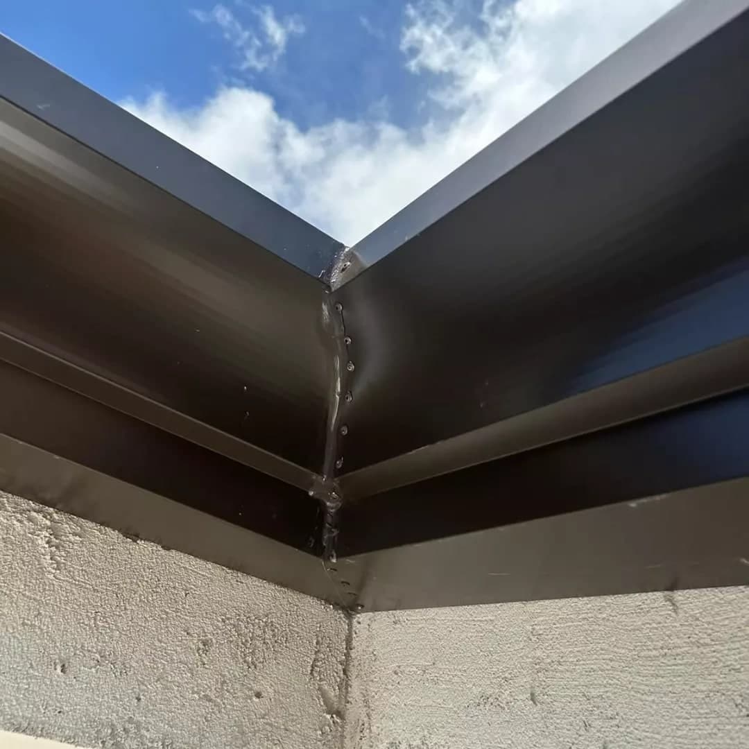 L’angolo interno di una gronda scura, visto da sotto contro il cielo.