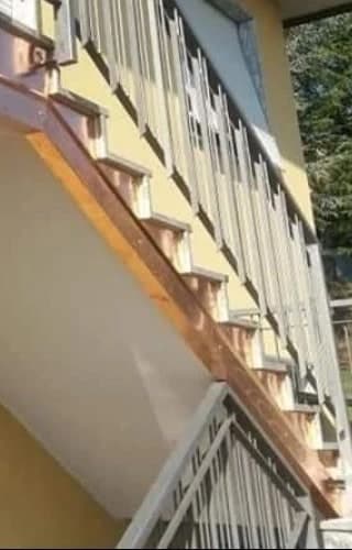 La scala da vicino: il fianco di ogni gradino rivestito di rame sotto la pedata in pietra, la fascia di rame lungo la soletta inclinata e la sua piega sotto, arancio; sopra, la ringhiera.