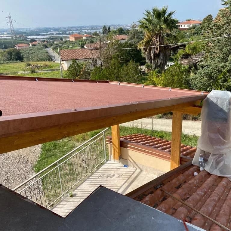 Il tetto visto dall’alto: la guaina ardesiata rossa sulla falda e il bordo color rame; sotto, il terrazzo e un tetto in tegole.