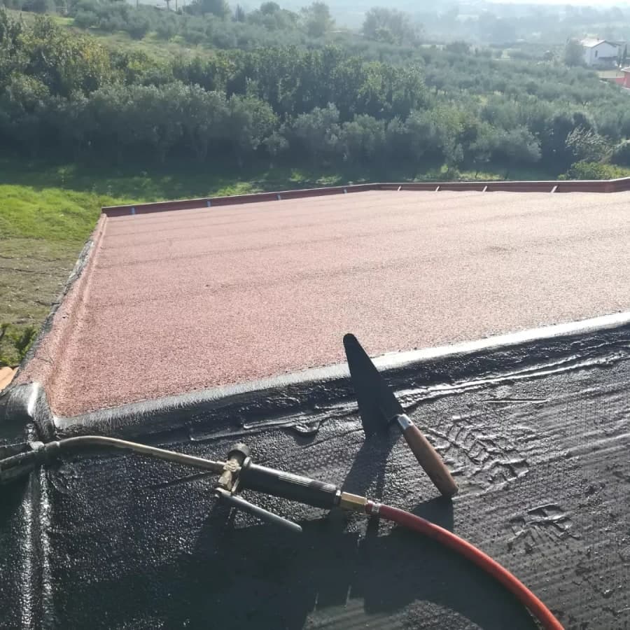La guaina in posa: il cannello sul primo strato nero, e oltre la guaina ardesiata rossa già stesa fino al bordo.