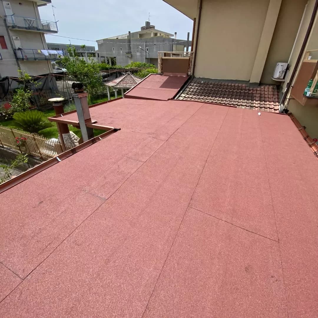 Il terrazzo finito, visto verso la casa: la guaina ardesiata rossa a teli, i bordi in lamiera color rame, un camino in acciaio con l’aspiratore; in fondo una falda in coppi.