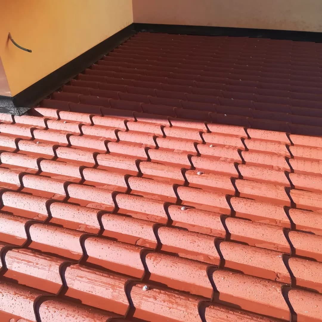 Le lastre finto coppo rosse della tettoia, in un angolo fra due muri gialli, con la scossalina scura che risale sul muro.