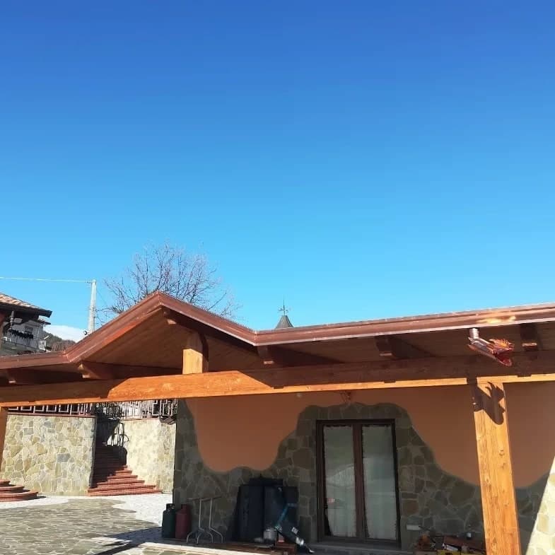 Il portico visto di lato: le travi chiare, la gronda in rame lungo il bordo e il frontone; all’angolo, un doccione in rame a testa di drago.