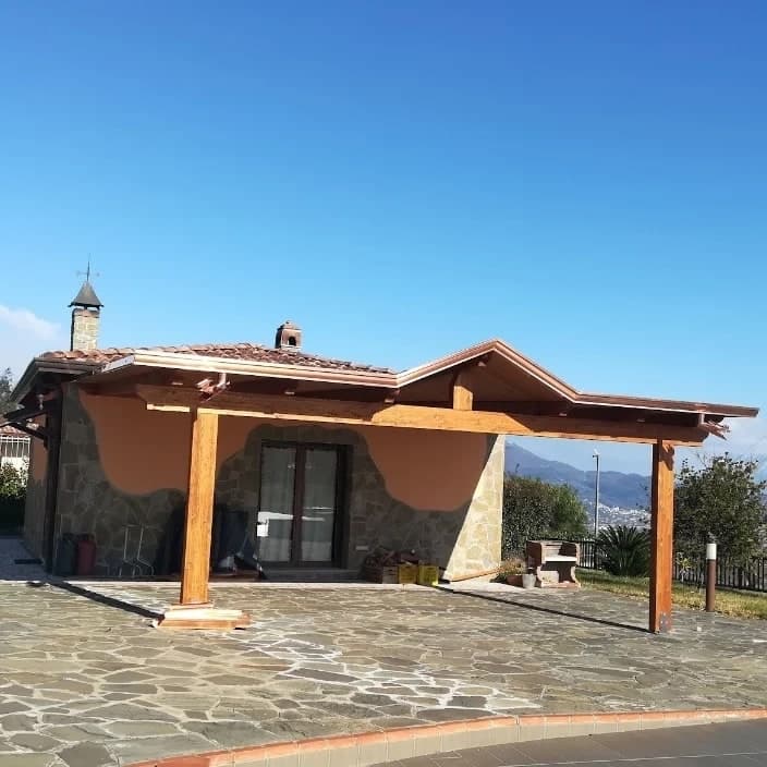 Il portico in legno di tre quarti, sul piazzale in lastre di pietra: lungo il bordo la gronda in rame, che sale anche sugli spioventi del frontone.