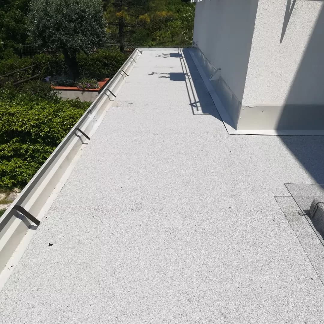 Dall’alto, la copertura finita: la guaina ardesiata grigio chiaro, la gronda grigia lungo il bordo con le staffe scure di traverso, la scossalina contro il muro della casa.