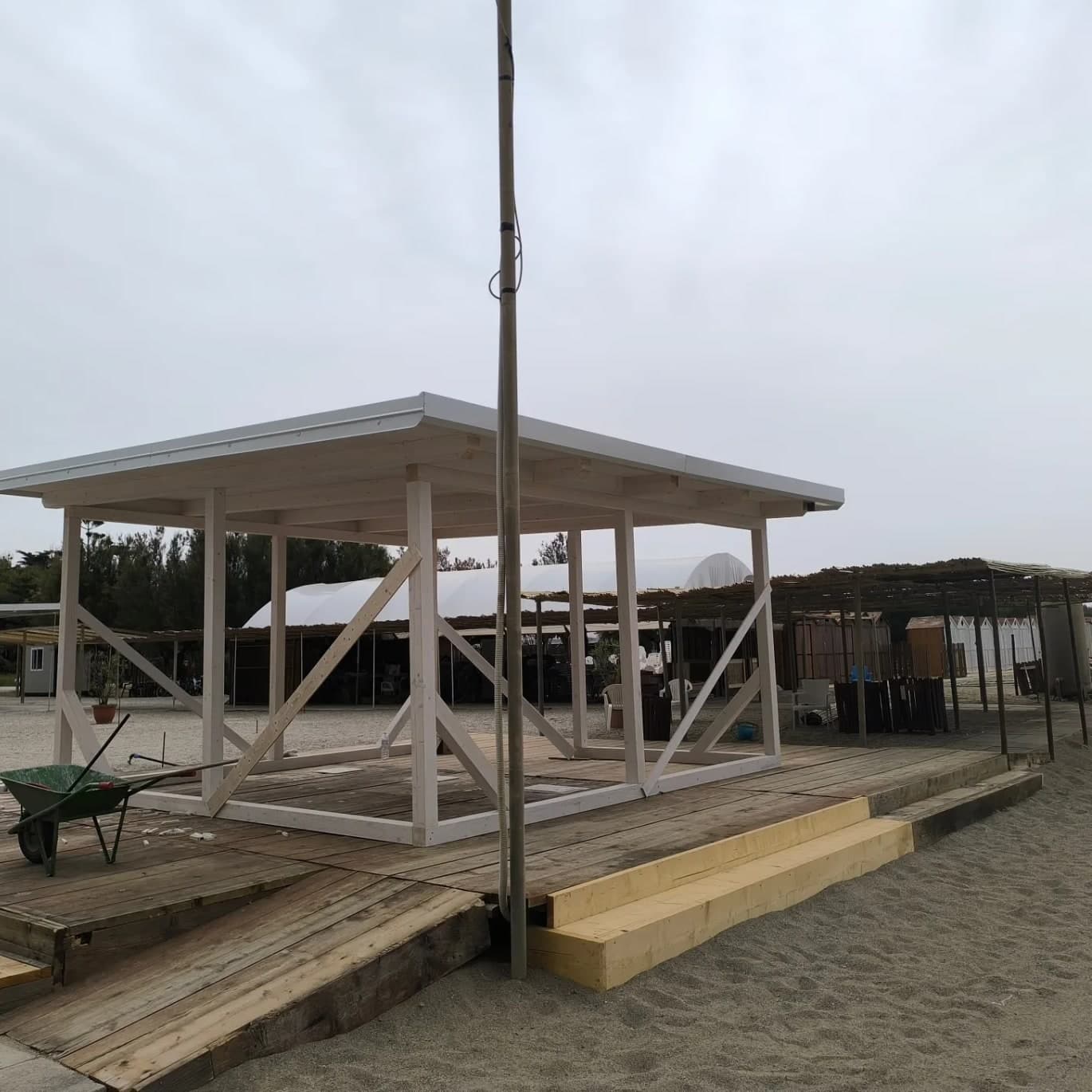 La struttura vista da un angolo, sulla pedana con i gradini nuovi: le croci a «V» sui due lati, i travetti e le tavole del tetto; dietro, le pergole e le cabine del lido.