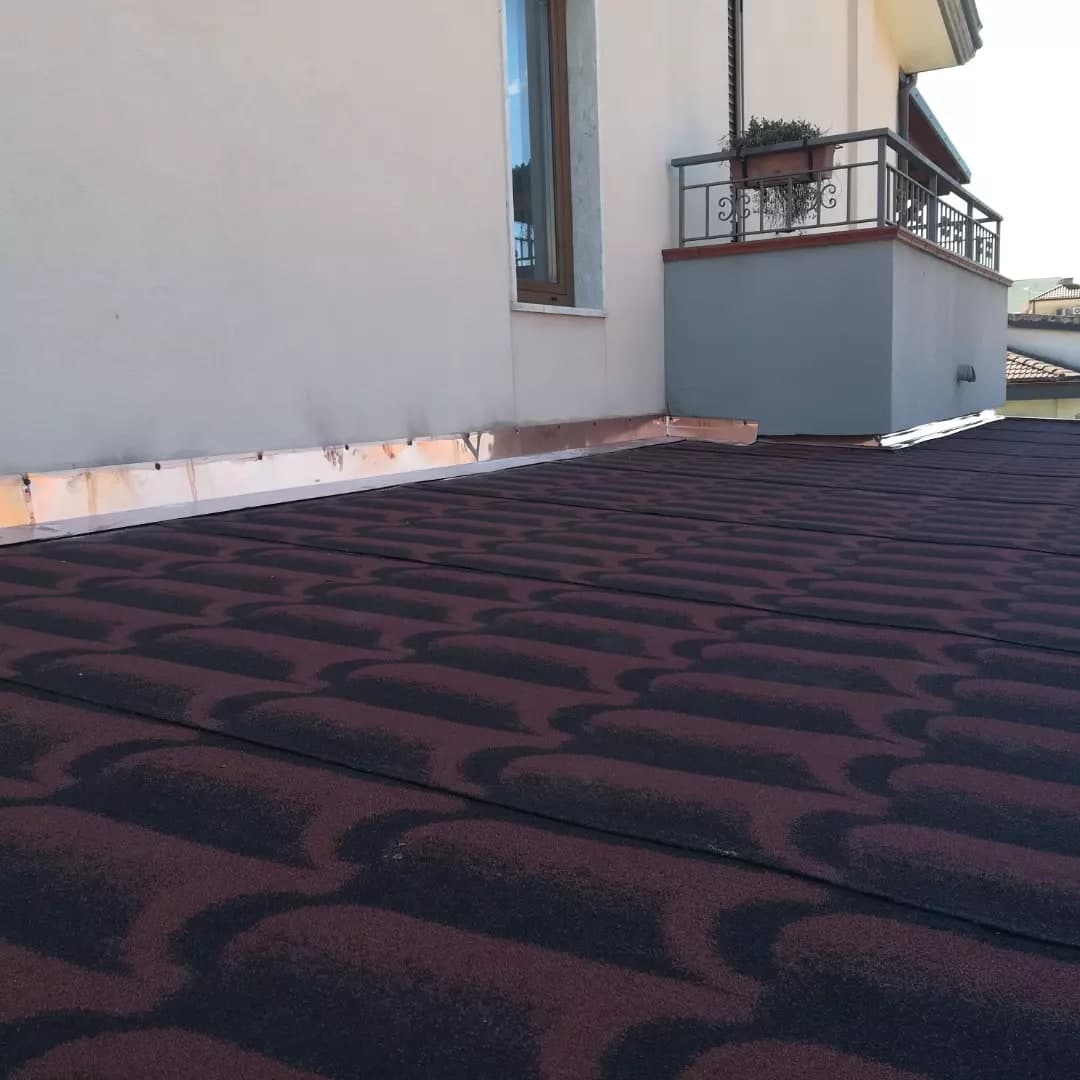 Il manto della tettoia, finito: la guaina rosso scuro stampata a coppi, e contro il muro la scossalina in rame fissata con una fila di chiodi, che gira attorno al balconcino grigio del piano di sopra.